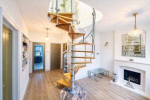 Bespoke spiral staircase with solid oak treads and a curved glass balustrade in a ground floor living space.